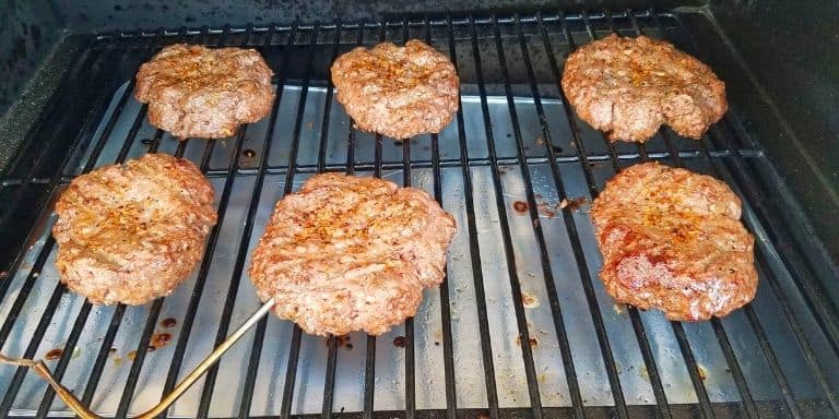 Six hamburgers on a grill with a meat thermometer